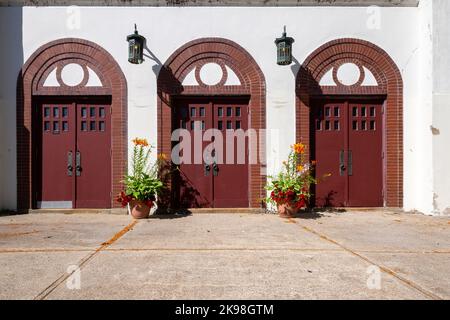 Three sets of red double doors with six small windows and a large door handle. The building is white stucco with vintage lanterns. Stock Photo