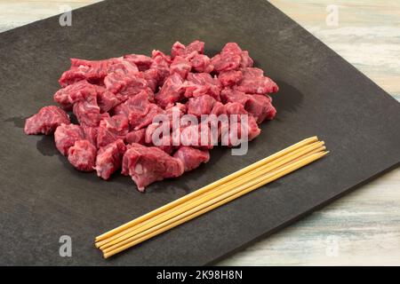 Raw beef bavette sirloin steak cubes and wooden skewers on black cutting board Stock Photo