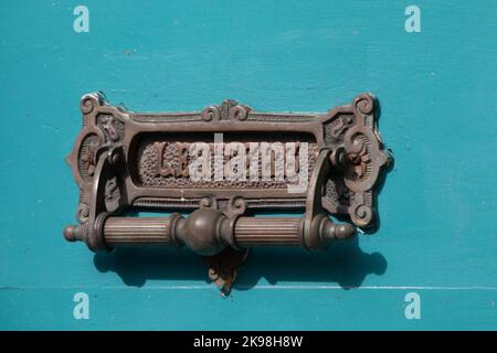 A vintage through the door mail slot and door knocker. The antique brass metal is distressed and embossed with stamped word letters. It is affixed Stock Photo