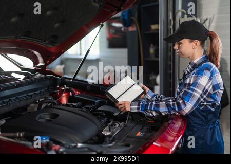 Caucasian female auto mechanic changes the engine air filter in the car. Stock Photo
