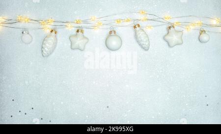 christmas decorations hanging on the rope of garland lights against silver background Stock Photo