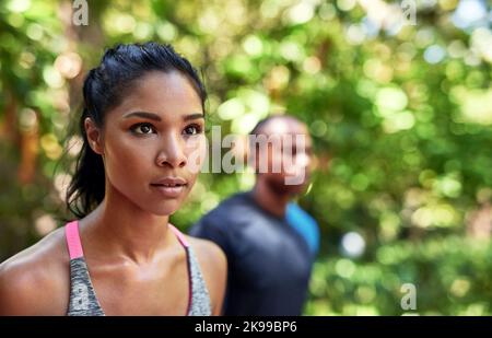 Were fully focused on achieving our fitness goals. an attractive young woman exercising outdoors with her boyfriend in the background. Stock Photo