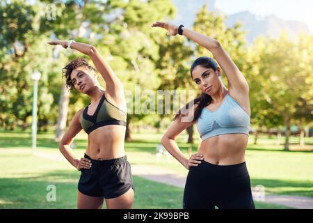 Breathe through it. two attractive young women stretching next to each other in the park during the day. Stock Photo