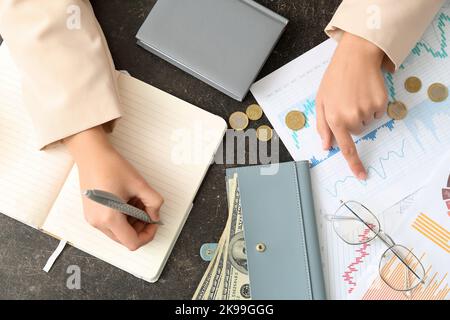 Woman with diagrams writing in notebook on dark table, top view. Budget concept Stock Photo