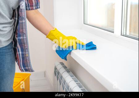 sanitizing service for office and home. Professional cleaner washing white windowsill in living room of apartment. female hands in gloves wipe white w Stock Photo