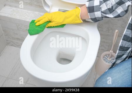 Servise cleaning toilet. Woman in yellow rubber gloves cleaning toilet seat with green cloth. Bathroom and toilet hygiene Stock Photo