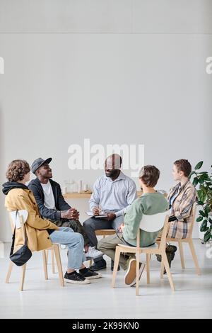 Group of students sitting on chairs with coach and discussing psychological moments at class Stock Photo