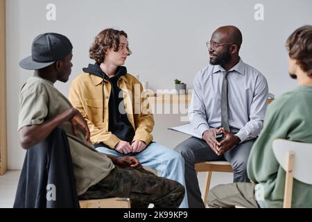 Group of students sitting on chairs and talking to their teacher during psychotherapy at class Stock Photo
