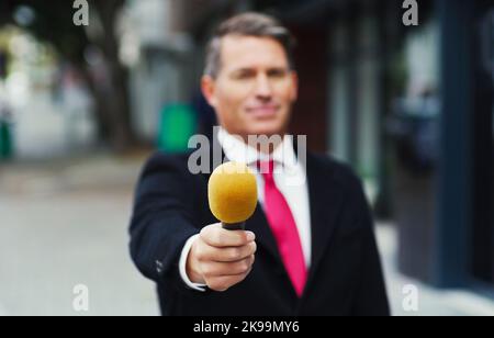 Any comments on the issue at hand. a mature male reporter holding out a microphone while doing an interview out in the city. Stock Photo