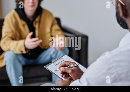 Close-up of African psychologist listening to patient and making notes during psychotherapy session Stock Photo