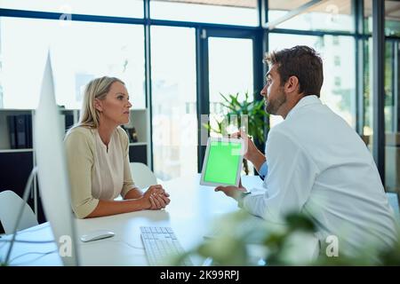 Technology bridges he gap between doctor and patient. a doctor using his digital tablet while consulting a female patient in his office. Stock Photo