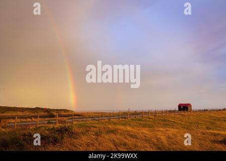 Rainbow after the storm at sunset over the red roofed hut Rye Harbour nature reserve on the East Sussex coast south east England UK Stock Photo