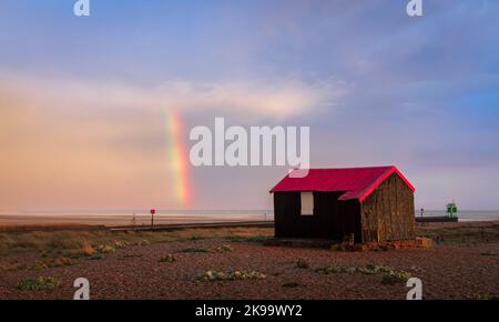 Rainbow after the storm at sunset over the red roofed hut Rye Harbour nature reserve on the East Sussex coast south east England UK Stock Photo