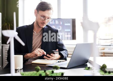 Serious businessman concentrating on his online work on mobile phone while working at table with laptop at office Stock Photo