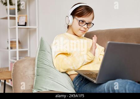 Portrait of teen girl with Down syndrome waving at camera in online lesson Stock Photo
