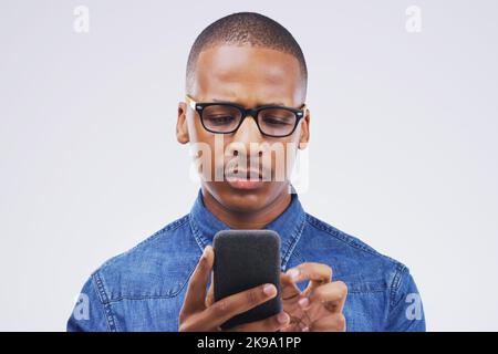 Hmm...I dont recognize this number. Studio shot of a young man using a mobile phone against a grey background. Stock Photo