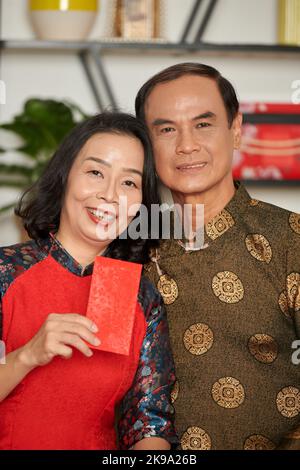 Portrait of happy senior couple holding red lucky money envelope they prepared for granchildren Stock Photo