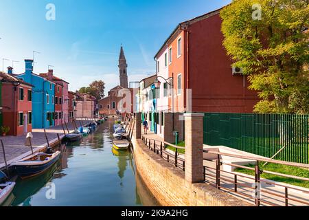 Canal with boats and colorful houses of the Burano Island in Venice, Italy. The Church of Saint Martin Bishop on the background. Stock Photo