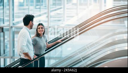 Shes excited about their new partnership. two young businesspeople having a chat while going up an escalator in a modern workplace. Stock Photo