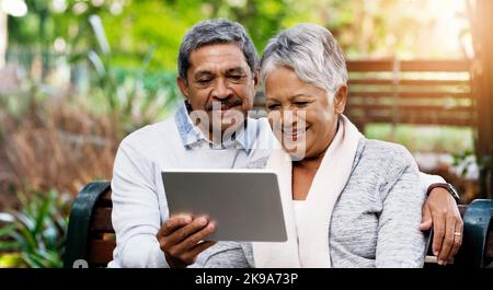 Watching some of our favorite videos together n the park. an affectionate senior couple using a digital tablet together while sitting on a bench Stock Photo
