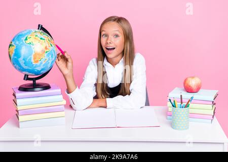 Photo of shocked intelligent schoolchild sit desk point pen continent map pass test isolated on pastel color background Stock Photo