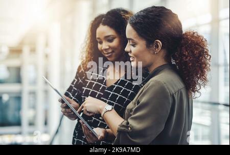 This is how high our numbers have gone. two attractive businesswomen using a digital tablet together while standing in a modern workplace. Stock Photo