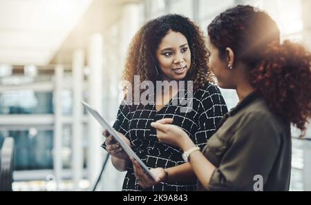 Technology is there to make collaboration simpler. two attractive businesswomen using a digital tablet together while standing in a modern workplace. Stock Photo