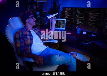 Profile portrait of funny bored hacker sit chair hand hold play paper plane night workstation indoors Stock Photo