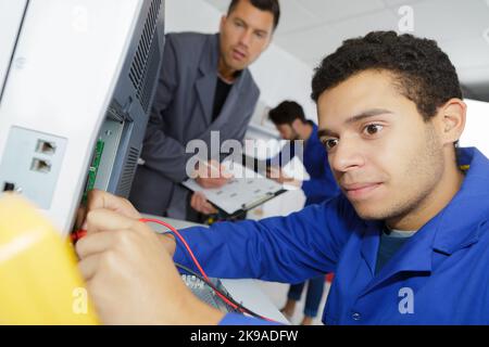 young apprentice electrician using multimeter on electrical appliance Stock Photo