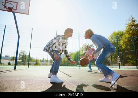 Group of friends bonding outdoors to play street basketball. Teens wearing casual style clothes. Kids look happy, delighted. Sport, energy, motion Stock Photo