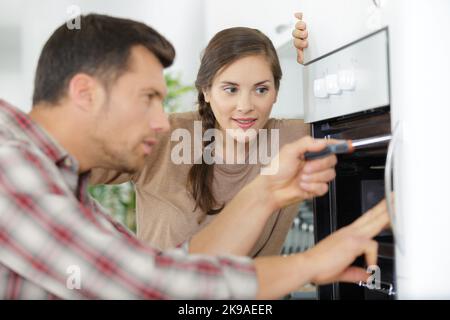 young woman looking at male worker repairing the oven Stock Photo