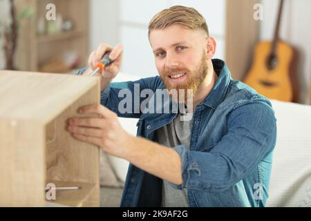man assembling furniture at home using a screwdriver Stock Photo