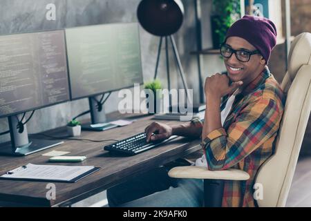 Photo of cheerful cool programmer wear spectacles hat working modern device indoors workplace workshop home Stock Photo