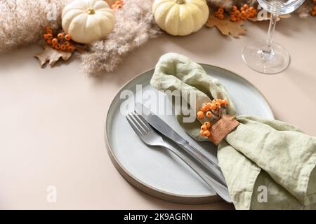 Thanksgiving day autumn table setting in natural colors decorated white pumpkin, orange berries on beige background. Close up. Copy space. Stock Photo