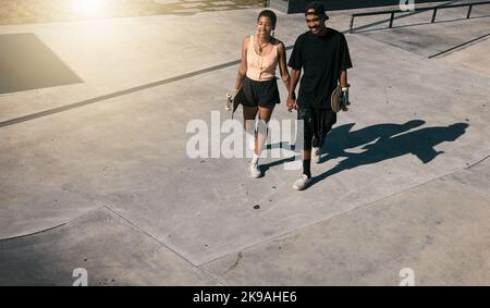 Couple, holding hands or walking on skatepark date in fun fitness, skating exercise or love bonding. Smile, happy man or skater woman and skateboard Stock Photo