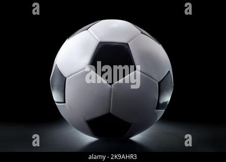 Detail view of classic black and white leather soccer ball isolated on table and black background. Front view. Stock Photo