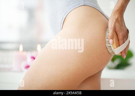 Cellulite treatment, woman arm holding dry brush to of her leg. Stock Photo