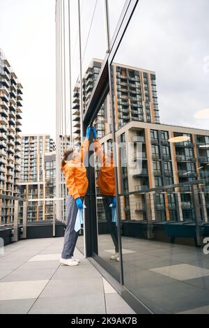 Cleaning lady cleans the mirrored windows of an office center Stock Photo