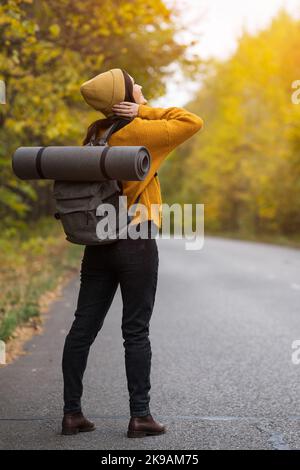 Young brunette woman with backpack stands on autumn road Stock Photo