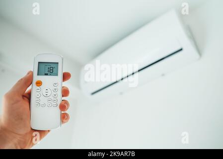 Hand holding remote control aimed at the air conditioner. Stock Photo