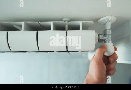 Male hand adjusting thermostat to turn on the radiator heater at home. Stock Photo