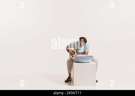 Portrait of young man sitting with dog and doing washing up isolated over white background Stock Photo