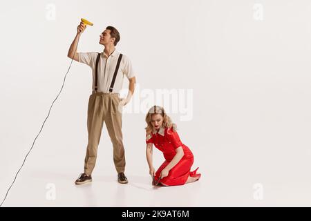 Portrait of young handsome man drying his hair while woman fixing with wrench isolated over white background Stock Photo