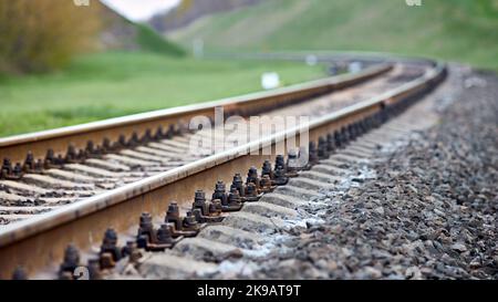 Selective focus railway track turns and twists between hills. Empty rounding and turning single track of railways. Shallow focus perspective view of Stock Photo