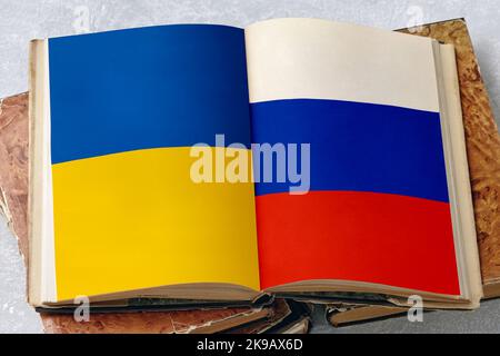 Ukrainian and Russian flags on the pages of an open vintage book, notepad, folder on a white concrete table Stock Photo