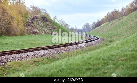 Selective focus railway track twists and turns between hills. Empty rounding and turning single track of railways. Shallow focus perspective view of Stock Photo