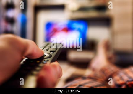Switching TV channels on TV with finger on remote controller Stock Photo