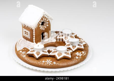 Isolated advent candlestick with lit first candle and christmas homemade gingerbread house on white background Stock Photo