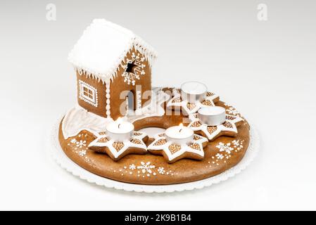 Isolated advent candlestick with two lighted candles and christmas homemade gingerbread house on white background. Stock Photo