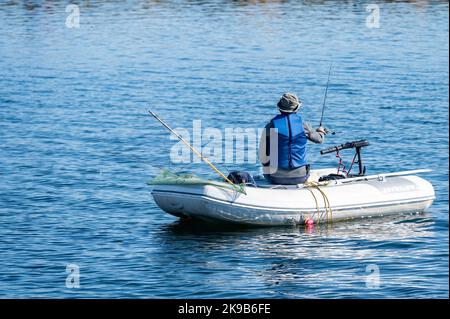 A lone man uses a Gala rubber boat and a rod to fish in Lake Simcoe. Stock Photo